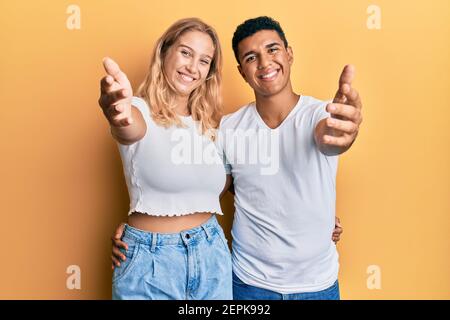 Giovane coppia interracial che indossa casual tshirt bianca sorridente amichevole che offre handshake come saluto e accogliente. Business di successo. Foto Stock