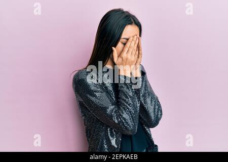 Giovane ragazza ispanica con giacca da festa con espressione triste che copre il viso con le mani mentre piange. Concetto di depressione. Foto Stock