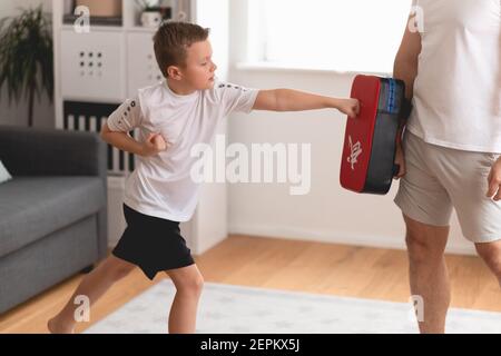 Un ragazzo di scuola giovane che esercita taekwondo a casa con il padre. Addestramento di papà e figlio. Allenamento domestico Foto Stock