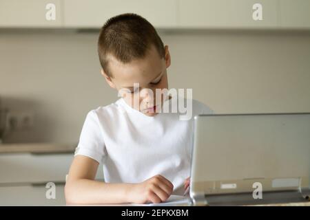 Boy 6-10 completa le lezioni scolastiche e i compiti online in cucina, guardando il computer tablet. Il concetto di istruzione a distanza. Rimani a casa. Foto Stock