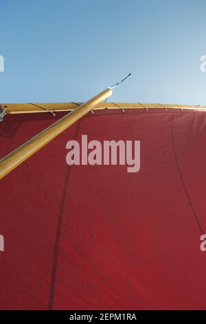 Guardando verso l'alto il rigging di un gaff trivellato barca a vela: Vela a vela rossa, albero di legno, borghi e cielo blu chiaro sopra Foto Stock