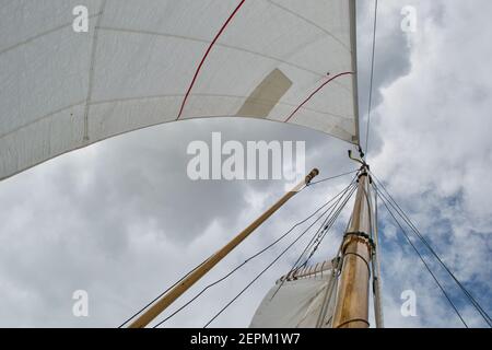 Guardando l'albero di uno yacht a vela rigato dalla pula: Vele bianche, albero di legno e pula, protezioni in corda, paralisi e fogli, e cielo blu nuvoloso e soleggiato Foto Stock