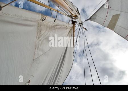 Guardando l'albero di uno yacht a vela rigato dalla pula: Vele bianche, albero di legno e pula, protezioni in corda, paralisi e fogli, e cielo blu nuvoloso e soleggiato Foto Stock