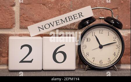 Data importante, novembre 26, stagione autunnale. Calendario fatto di legno su uno sfondo di un muro di mattoni. Sveglia retrò come concetto di gestione dell'ora. Foto Stock