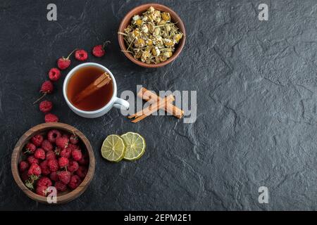 Tazza di tè con lamponi freschi e camomilla su nero sfondo Foto Stock