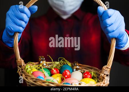 Persona che tiene il cestino di Pasqua che indossa guanti di protezione blu e maschera facciale, festa 2021 in tempo di scoppio globale di Coronavirus COVID-19 Foto Stock