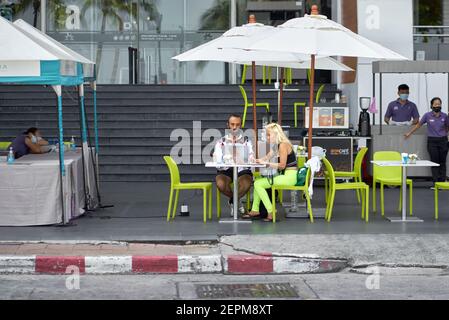 Una coppia che usa un computer portatile si è seduta in un bar con un pavimento di strada con una donna che indossa leggings verdi colorati. Thailandia Sud-est asiatico Foto Stock
