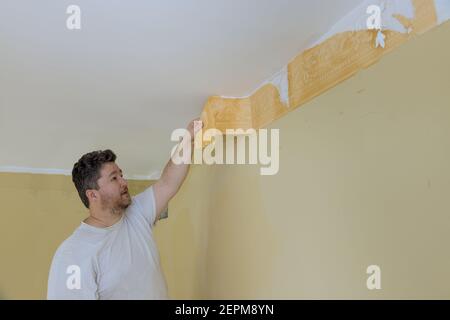 Man il processo di aggiornamento del muro rimuovendo la mano strappare la vecchia carta da parati dalla parete preparandosi per la riparazione domestica lavorare con una spatola Foto Stock