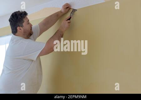 Preparazione per lavoro di riparazione a casa uomo mano strappare vecchio carta da parati da parete Foto Stock