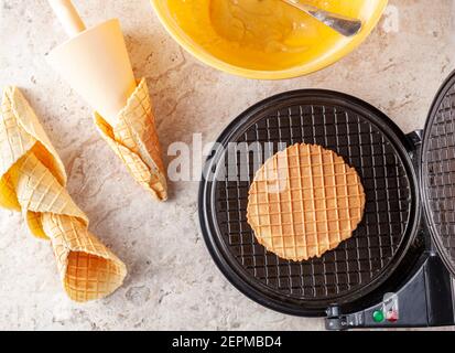 Immagine piatta della macchina a cono per cialde antiaderente per creare coni di gelato fatti in casa. I coni fatti a mano sono giacenti sul controsoffitto in marmo. Ingredien Foto Stock