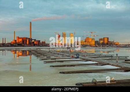 Finlandia, Helsinki 26 febbraio 2021 visione della centrale elettrica di cogenerazione a carbone Hanasaari Thaw, riflesso nell'acqua. Raggi luminosi al tramonto. La baia in primo piano. Mare primavera paesaggio. Foto di alta qualità Foto Stock