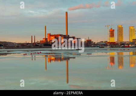 Finlandia, Helsinki 26 febbraio 2021 visione della centrale elettrica di cogenerazione a carbone Hanasaari Thaw, riflesso nell'acqua. Raggi luminosi al tramonto. La baia in primo piano. Mare primavera paesaggio. Foto di alta qualità Foto Stock