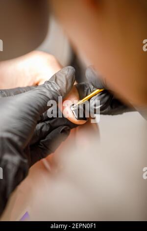 In un salone di bellezza, il maestro fa una manicure, applica un modello al chiodo con un pennello, vernice nera con un motivo dorato. Foto Stock