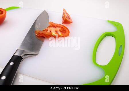 Su un tagliere c'è un pomodoro fresco tagliato rosso e un grande coltello da chef. Su uno sfondo bianco isolato. Foto Stock