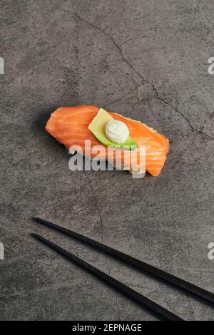 Alto angolo di sushi nigiri gustoso con fetta di salmone su riso condito con una sottile fetta di avocado e crema formaggio servito vicino a chopsticks Foto Stock