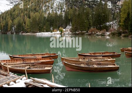 Scenario di barche in legno ormeggiate su un lago tranquillo increspato circondato da montagne innevate e alberi di conifere Foto Stock