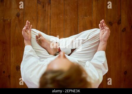 Da sopra raccolto anonimo maschio in vestiti bianchi facendo mudra gesto con le mani mentre si pratica yoga in casa Foto Stock