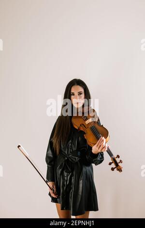 Un artista serio che suona uno strumento musicale a corde mentre pratica le abilità in piedi su sfondo bianco Foto Stock