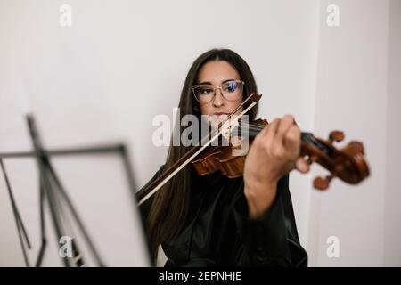 Un artista serio che suona uno strumento musicale a corde mentre pratica le abilità in piedi su sfondo bianco Foto Stock