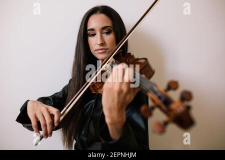 Un artista serio che suona uno strumento musicale a corde mentre pratica le abilità in piedi su sfondo bianco Foto Stock