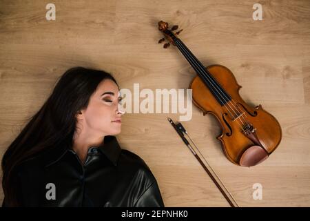 Donna e violino acustico moderno e arco di design classico posto su superficie di legno in studio musicale Foto Stock