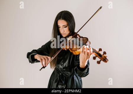 Un artista serio che suona uno strumento musicale a corde mentre pratica le abilità in piedi su sfondo bianco Foto Stock