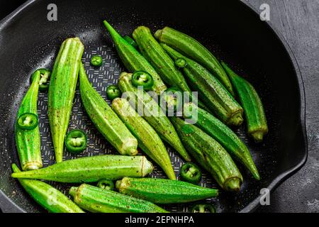 Da sopra l'okra fresco strappato sulla padella con il verde pepe su fondo scuro Foto Stock