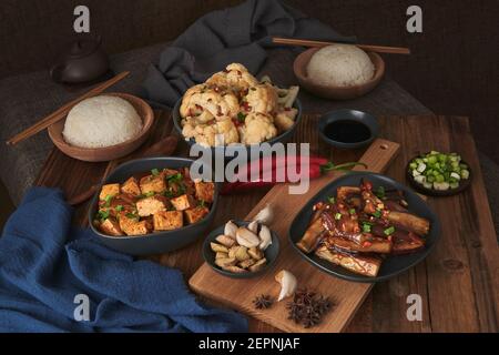 Mala tofu e yuxiang, piatti vegani cinesi, accompagnati da una ciotola di riso, cavolfiore, salsa di soia e una teiera giapponese in cima a un tavolo deco in legno Foto Stock