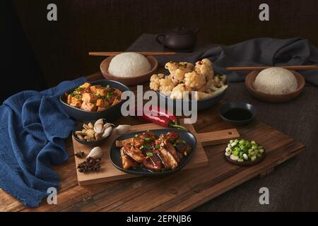 Mala tofu e yuxiang, piatti vegani cinesi, accompagnati da una ciotola di riso, cavolfiore, salsa di soia e una teiera giapponese in cima a un tavolo deco in legno Foto Stock