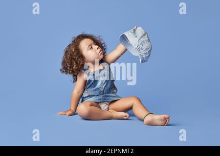 Adorabile bambino sconvolto con occhi marroni che indossano abiti casual e cappello su sfondo blu guardando via Foto Stock