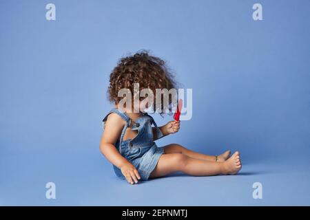 Vista laterale del corpo della bambina sconvolta in estate vestiti barefoted seduta con gelato su sfondo blu studio Foto Stock