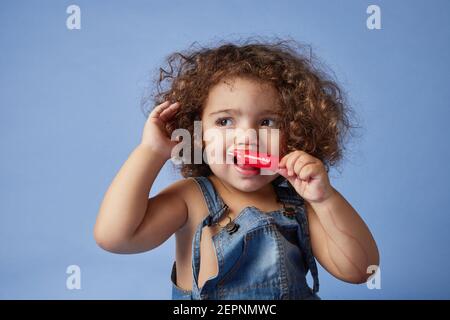 Ragazza piccola sconvolta che guarda via in piedi con gelato contro studio sfondo blu Foto Stock