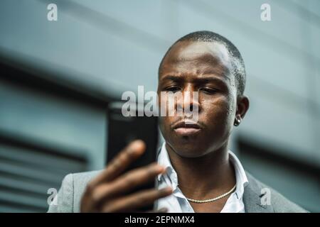 Grave boss nero maschio che naviga in un cellulare in città Foto Stock