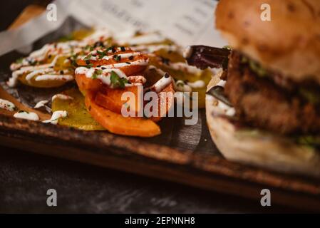 Primo piano di hamburger yummy con paty vegetariano e alla griglia shiitakes tra le ciambelle vicino patate dolci e le fette di carota con salsa di alioli su sfondo scuro Foto Stock