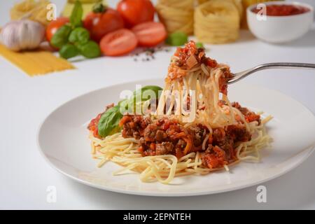 Spaghetti tradizionali italiani bolognesi serviti su un piatto bianco con pomodori e basilico Foto Stock