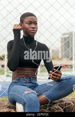 Nero a capelli corti Donna che ascolta musica con un telefono cellulare e cuffie Foto Stock