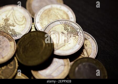 Profondità di campo poco profonda (fuoco selettivo) e immagine macro con una moneta da 2 euro in metallo vicino ad altre monete in euro su sfondo nero. Foto Stock