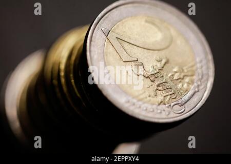 Profondità di campo poco profonda (fuoco selettivo) e immagine macro con una moneta da 2 euro in metallo vicino ad altre monete in euro su sfondo nero. Foto Stock