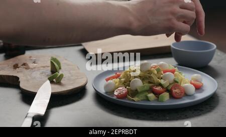 L'uomo slow motion aggiunge mozzarella al pesto fettuccine su piatto blu, foto ampia Foto Stock