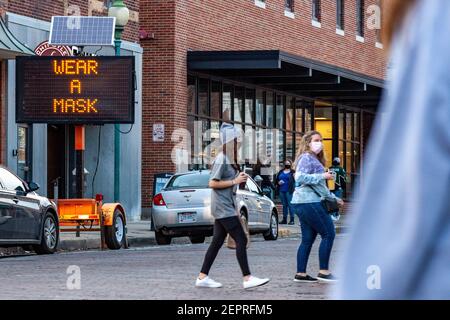 Atene, Stati Uniti. 27 Feb 2021. Il cartello pubblico di Atene che dice indossare una maschera mentre la gente attraversa la strada. Mentre il tempo in Ohio scalda gli studenti dell'Ohio University, dirigiti verso Court Street per socializzare ai bar. La distribuzione dei vaccini è ancora in corso in Ohio, ma per gli studenti che non interagiscono con molti individui al di fuori della loro coorte la minaccia della malattia del coronavirus (COVID-19) non ha impedito loro di uscire per una notte in città. Credit: SOPA Images Limited/Alamy Live News Foto Stock