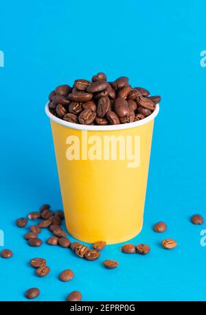 chicchi di caffè in un bicchiere giallo su sfondo blu Foto Stock