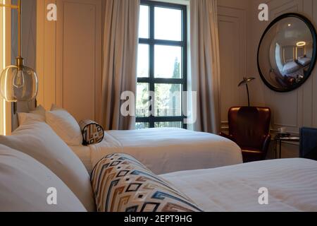 Una camera da letto accogliente e moderna di lusso con letti gemelli, una lussuosa e confortevole sedia con tappezzeria in pelle rossa e uno specchio sferico Foto Stock