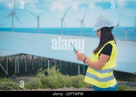 l'ingegnere femminile adulto supervisiona i pannelli solari e mulini a vento in un energia rinnovabile complesso Foto Stock