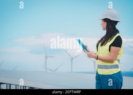 l'ingegnere femminile adulto supervisiona i pannelli solari e mulini a vento in un energia rinnovabile complesso Foto Stock