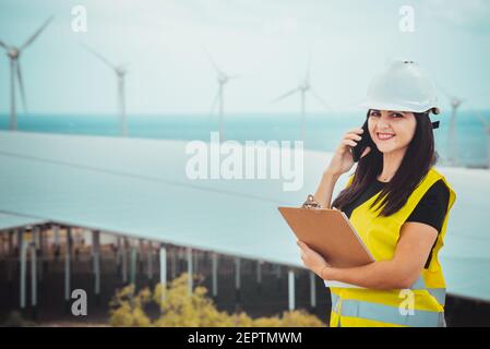 l'ingegnere femminile adulto supervisiona i pannelli solari e mulini a vento in un energia rinnovabile complesso Foto Stock