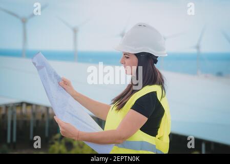 l'ingegnere femminile adulto supervisiona i pannelli solari e mulini a vento in un energia rinnovabile complesso Foto Stock