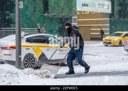 Mosca. Russia. 12 febbraio 2021. Un addetto alla pubblica utilità rimuove la neve con uno scraper su una strada cittadina durante una nevicata in una giornata invernale. labo fisico duro Foto Stock