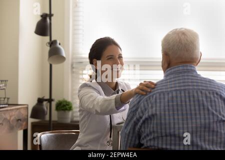 Vista posteriore sorridente dottore femminile che conforta l'uomo maturo, toccando la spalla Foto Stock