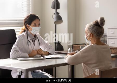 Medico indossando maschera di faccia che consulta donna matura al meeting Foto Stock