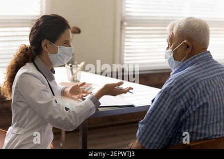 Vista laterale femmina sorridente medico indossando maschera di consulenza vecchio uomo Foto Stock